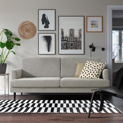 Modernes Wohnzimmer mit grauem GRILLSTORP-Sofa, Schwarz-Weiß-Dekor, Couchtisch aus Holz, Kunstwerken und Pflanzen.