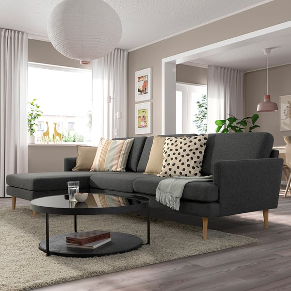 Modernes Wohnzimmer mit grauem GRILLSTORP-Sofa, gemusterten Kissen, rundem Couchtisch, großem Fenster und Dekor.