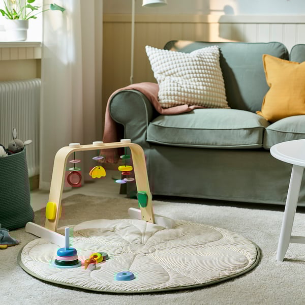 Gemütliches Wohnzimmer mit hellblauem Sofa, buntem Baby-Aktivitätsbogen und runder, gesteppter weißer Decke auf dem Boden.