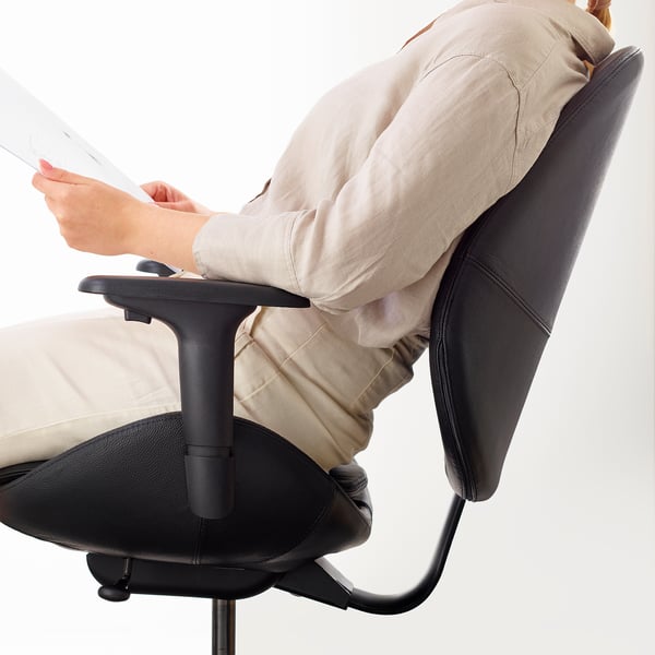 Bildbeschreibung: Eine Person, die auf einem ergonomischen Bürostuhl sitzt und ein Dokument liest. Der Stuhl hat verstellbare Armlehnen und eine gut geformte Rückenlehne.