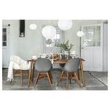 Moderne Essgarnitur mit drei grauen Stühlen und einem hellen Tisch. Über den Köpfen hängen weiße Papierlaternen. Einfaches und elegantes Design.