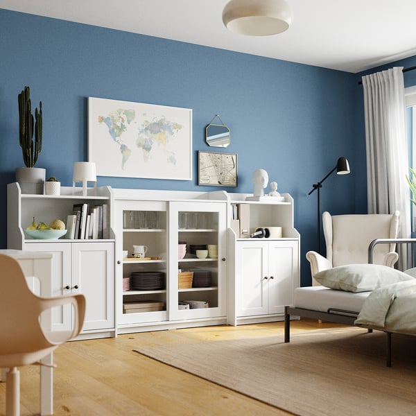 Helles Wohnzimmer mit blauen Wänden, weißen Möbeln und einem Poster auf der Weltkarte. Ein gemütlicher Sessel mit einer Stehlampe und Holzboden.