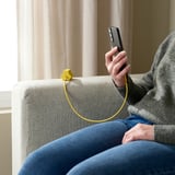 Person auf der Couch mit Telefon, HAVSKÅL Kabelorganisator, Freizeitkleidung, Vorhänge hinten.