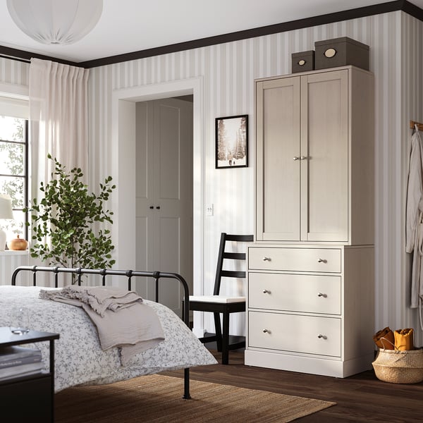 Gemütliches Schlafzimmer mit HAVSTA-Schrank, Truhe, Bett und Pflanze. Hochschrank mit Stuhl, Truhe mit Korb, sanfte Beleuchtung, großes Fenster.