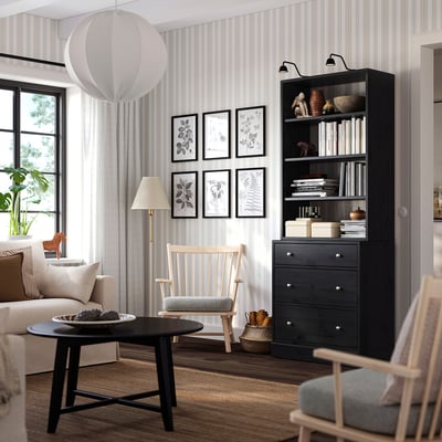 Modernes Wohnzimmer mit schwarzem Bücherregal, Schaukelstuhl und großem Fenster.