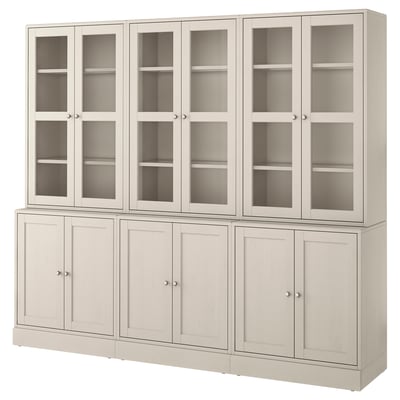 Ein hellgrauer Holzschrank von HAVSTA mit Glastüren und Schubladen aus Massivholz.