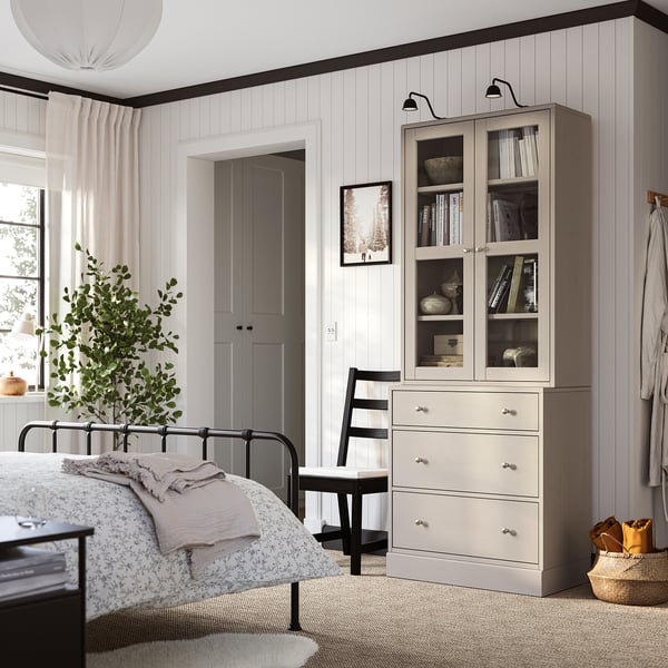 Rustikal-modernes Schlafzimmer mit HAVSTA-Möbeln, Glasvitrine, schwarzem Bett, Pflanze, Stuhl.