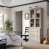 Rustikal-modernes Schlafzimmer mit HAVSTA-Möbeln, Glasvitrine, schwarzem Bett, Pflanze, Stuhl.