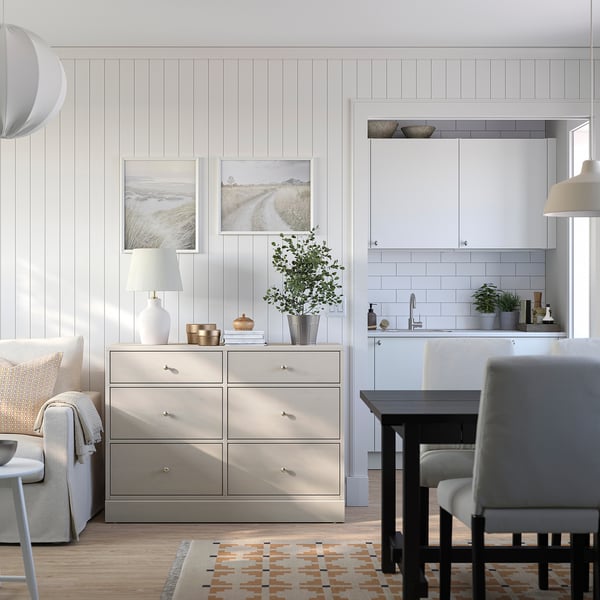 Modernes Wohnzimmer mit HAVSTA-Schubladen, weißer Küche, beigem Sofa, schwarzem Esstisch und gemustertem Teppich.
