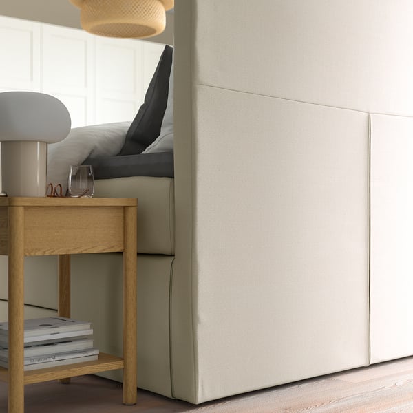 Schlafzimmer mit HEMFJÄLLET-Schlafcouch mit Schubladen und bequemem Kopfteil. Auf dem Nachttisch stehen Bücher und eine Lampe.