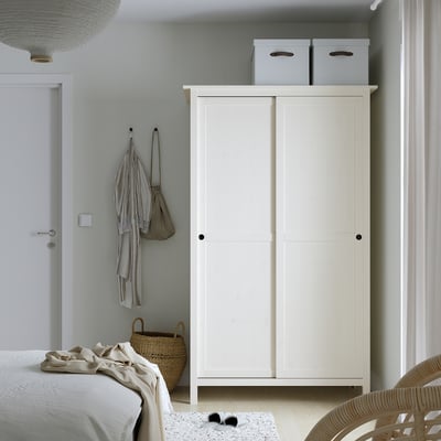 HEMNES Kleiderschrank: hoch, weiß, Schiebetüren, Platten mit 2 grauen Kästen. Neben dem Bett, über dem Korb, Stuhl.