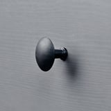 Kleiner schwarzer runder Haken an einer strukturierten grauen Wand.