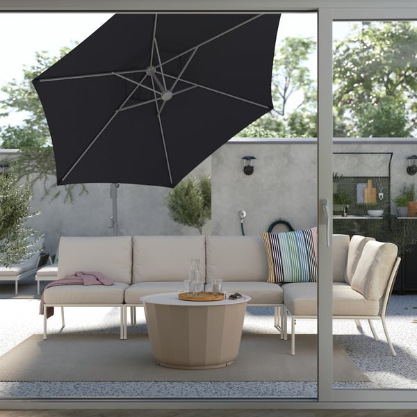Moderne Terrasse mit schwarzem HISSÖ-Sonnenschirm, weißem Lounge-Set, rundem Tisch, Kissen und grünen Kissen auf gemustertem Teppich.
