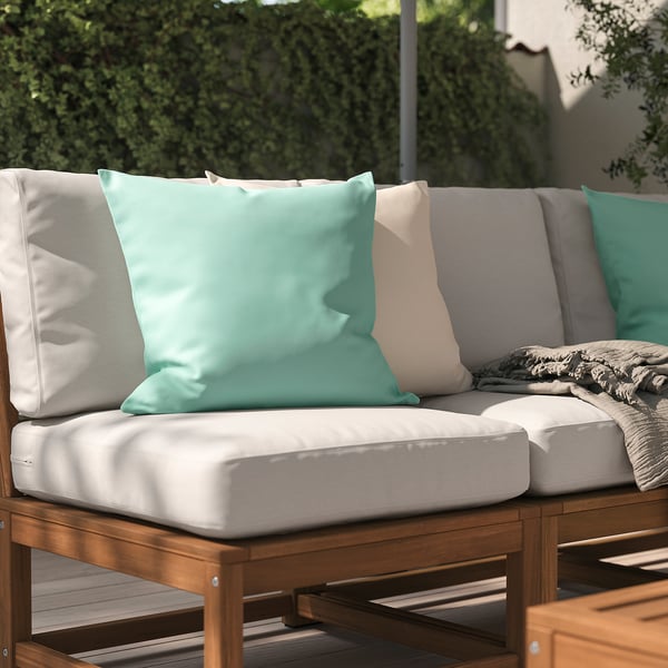 Ein hellblaues Outdoor-Kissen namens HJÄRTERÖ auf einem beigen Sofa im Freien.
