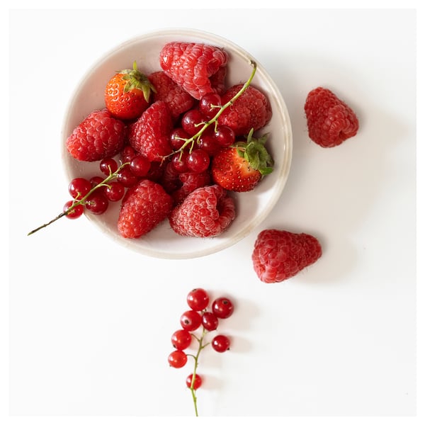 Schüssel mit roten gemischten Beeren, darunter Erdbeeren, Himbeeren und rote Johannisbeeren, auf weißer Oberfläche.