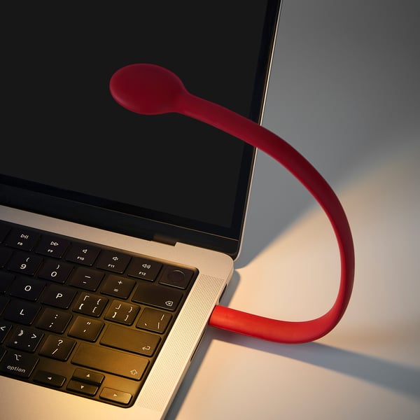 Rote HÖSTULOTA Lampe auf Laptop; Schlankes, geschwungenes Design.