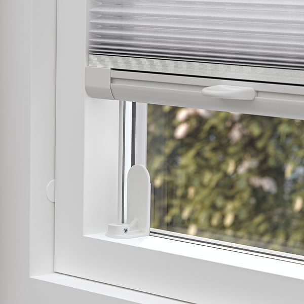 Ein Fenster mit teilweise geöffnetem Plissee, das aus Sicherheitsgründen kabellos bedient werden kann. Die Jalousie filtert das Licht und sorgt für Privatsphäre.