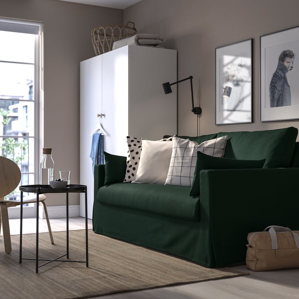 Modernes Wohnzimmer mit grünem HYLTARP-Sofa, großer Kunst, elegantem Tisch, gemütlichem Teppich und weißem Stauraum.