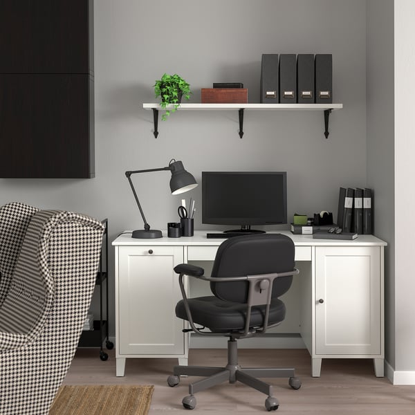 Home-Office-Einrichtung mit weißem IDANÄS-Schreibtisch, schwarzem Stuhl, Monitor, Lampe und Regal mit Büchern und Pflanzen.
