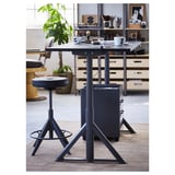 Ein moderner, höhenverstellbarer Schreibtisch mit grauer Platte, Metallbeinen und schwarzem Drehstuhl. Der Schreibtisch ist von Büromöbeln und Pflanzen umgeben.