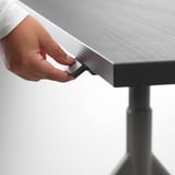 Eine Hand, die die Höhe eines Schreibtisches mit einem Griff einstellt und seine verstellbare Funktion demonstriert.