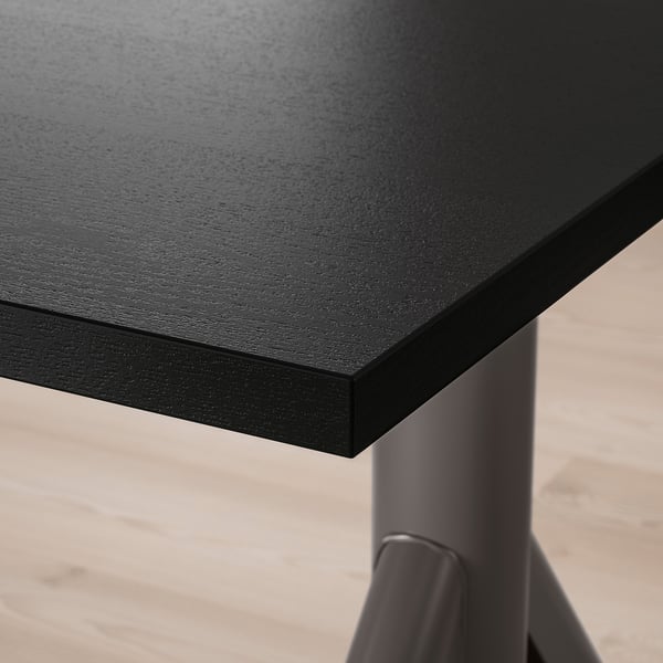 Nahaufnahme eines modernen, schwarzen Schreibtisches mit glatter, langlebiger Oberfläche und robusten Metallbeinen, der hochwertige Materialien und Design präsentiert.