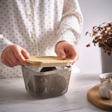 Eine Person öffnet einen IKEA 365+ Futterkorb mit Holzdeckel auf einer Küchentheke.
