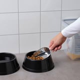 Person schöpft Hundefutter aus dem Beutel in die Schüssel mit einer Edelstahlschaufel.