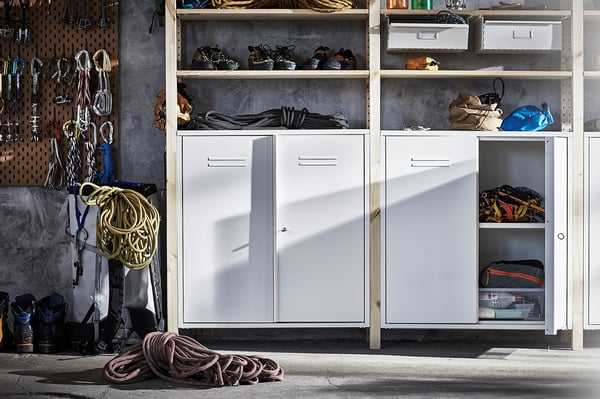 Weiße IVAR-Schränke und Regale organisieren Kletterausrüstung an einer grauen Wand, mit Haken, die Seile und Helme halten.