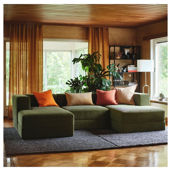 Grünes modulares Sofa mit orangefarbenen Kissen in der Nähe großer Fenster, Holzdekor.