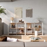 Minimalistischer Wohnbereich in neutralen Tönen, mit Holzregalen mit verschiedenen Dekorationsgegenständen, einem beigen Sofa und abstrakter Wandkunst.