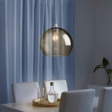 Moderner Essbereich mit einer Pendelleuchte aus rauchfarbenem Glas über einem Tisch, der mit einem Holztablett, einer Karaffe und Gläsern gedeckt ist und für Umgebungsbeleuchtung sorgt.