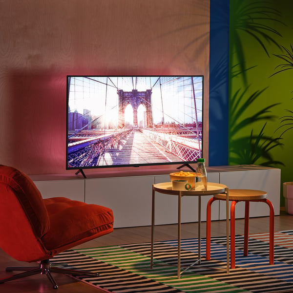 Modernes Fernsehzimmer mit farbenfrohem Dekor, großem Bildschirm, orangefarbenem Stuhl, lebendigen Wänden, LED-Beleuchtung, kleinem Tisch mit Snacks.