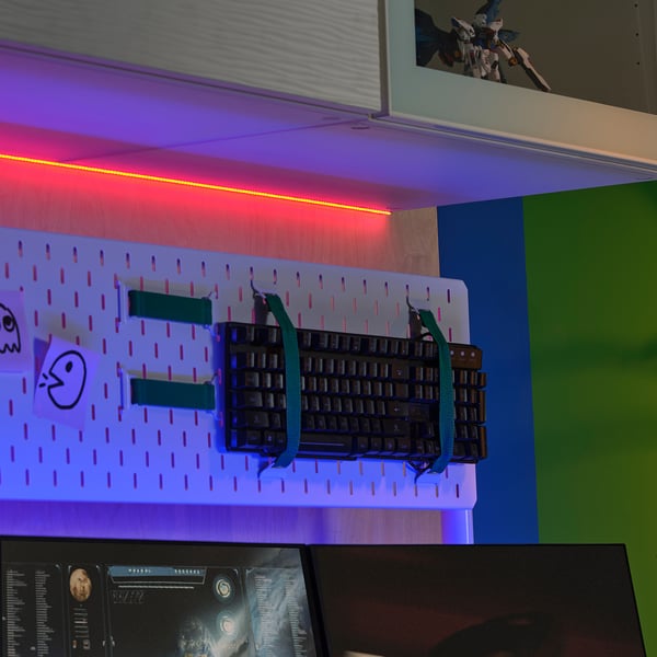 An der Wand montierte Stecktafel mit Tastatur, Aufklebern und bunten LED-Leuchten. Kleine Actionfigur im Regal.