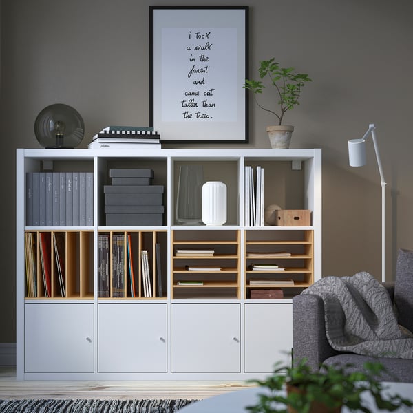 Modernes Wohnzimmer mit KALLAX Regal, Büchern, Dekor, grauer Couch und Decke.