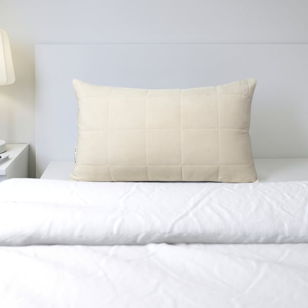 Ein rechteckiges beiges Kissen mit Steppmuster liegt auf einem weißen Bett. Das Kissen hat eine kühlende blaue Seite und eine wärmende beige Seite für abwechslungsreichen Komfort.