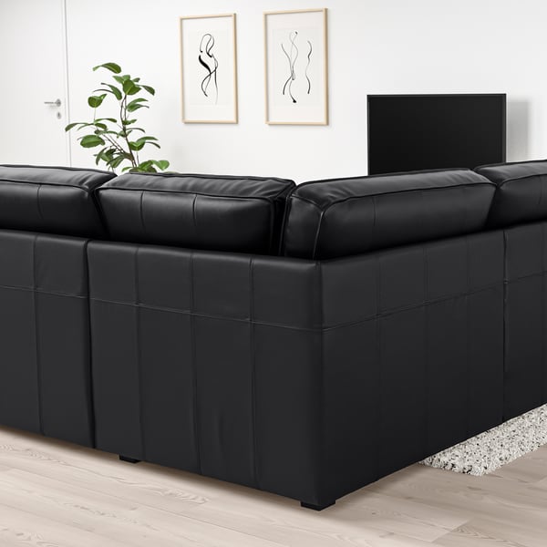Modernes Wohnzimmer mit großem schwarzem KIVIK-Ledersofa, breiten Armlehnen, Flachbildfernseher und Pflanze. Die Größe der Sofas dominiert den Raum.