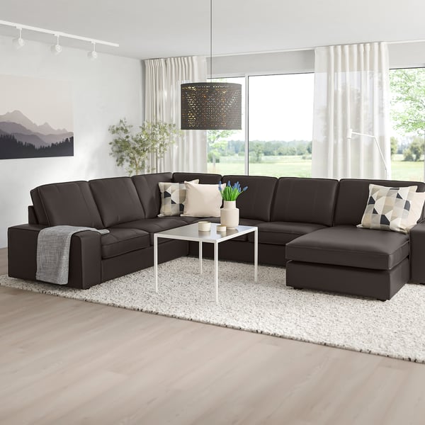 KIVIK Sektionssofa mit Kissen im modernen Wohnzimmer, niedrige Armlehnen, Plüschsitze, Couchtisch auf Teppich, Tageslicht, minimalistische Einrichtung.