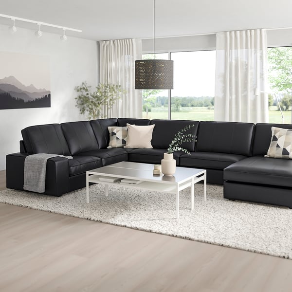 Modernes Wohnzimmer mit großem schwarzen KIVIK-Sofa, weißem Couchtisch und großen Fenstern. Schlankes, minimalistisches Design zum Entspannen.