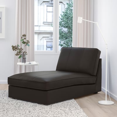 Modernes Wohnzimmer mit schwarzer KIVIK Chaiselongue, Stehleuchte und Beistelltisch. Großes Fenster mit weichen Vorhängen dahinter.