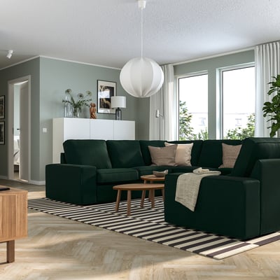 Modernes Wohnzimmer mit grünem KIVIK-Sofa, gestreiftem Teppich, Couchtisch, Pendelleuchte, großen Fenstern, blauen Wänden, weißem Schrank und Dekor.