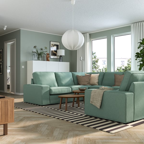 Ein gemütliches Wohnzimmer mit einem großen grünen KIVIK-Sofa, einem Teppich und großen Fenstern.