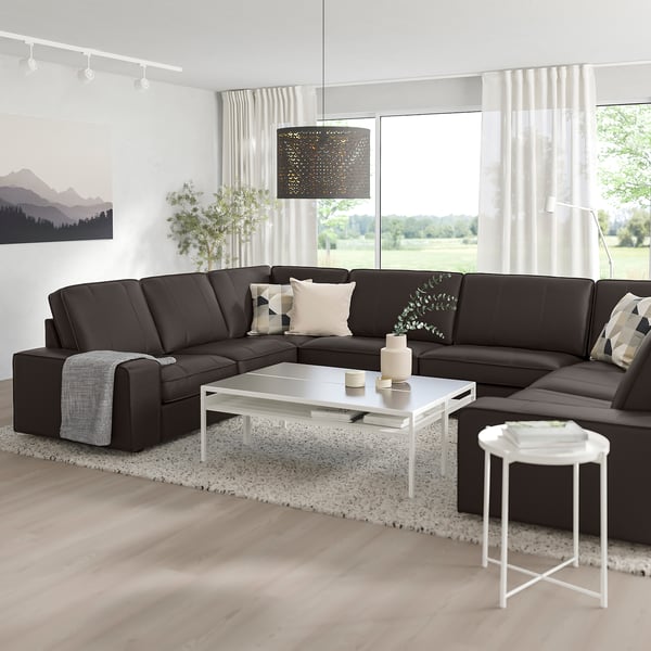 Modernes Wohnzimmer mit großem l-förmigem dunkelgrauem KIVIK-Sofa, weißem Couchtisch und großem Fenster. Sauberes und gemütliches Design.