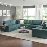 Modernes Wohnzimmer: großes blaugrünes, l-förmiges KIVIK-Sofa, dunkler Couchtisch, weißer Teppich, großes Fenster, graue Wände.