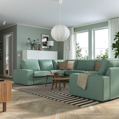 Modernes Wohnzimmer mit KIVIK Sofa in Blaugrün, Naturholzboden, gestreiftem Teppich und weißer Pendelleuchte. Das Sofa ist geräumig und passt gut zu großen Fenstern.