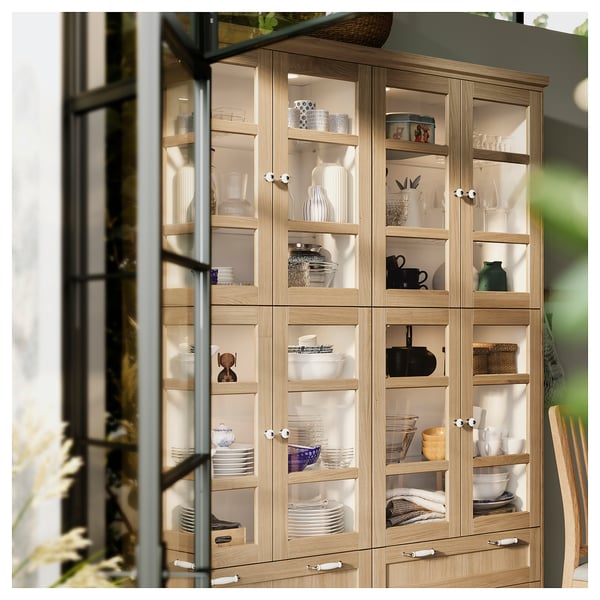 Holzschrank mit Glastüren, in dem Geschirr ausgestellt ist. Weiße Knöpfe und Porzellanakzente, ordentlich organisiert.