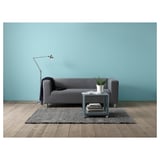 Modernes graues Sofa an blauer Wand, mit Decke, Pflanze, Büchern und Lampe.