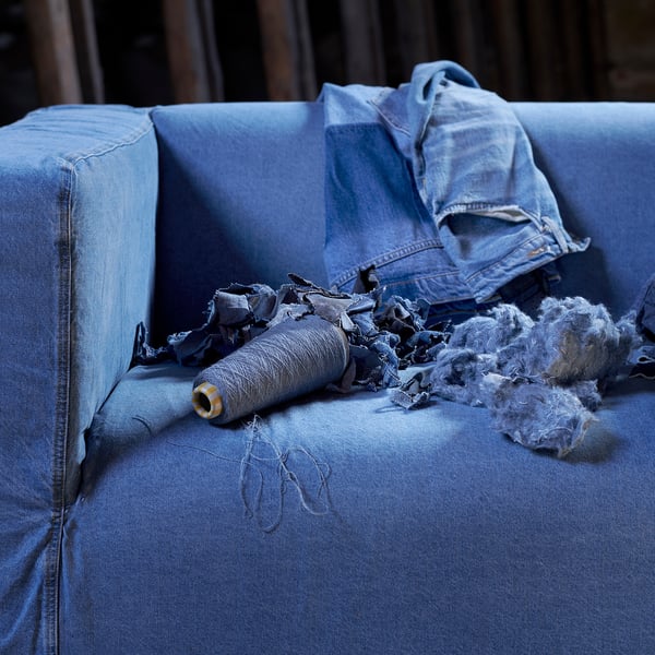 Blauer Denim-Sofabezug mit losen Fäden und Jacke, der abgenutzte Jeans zeigt, die zu Möbeln umfunktioniert wurden.