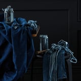 Blaue Denim-Jeans, drapiert über schwarzen Möbeln mit einem Glasgefäß auf dunklem Hintergrund.