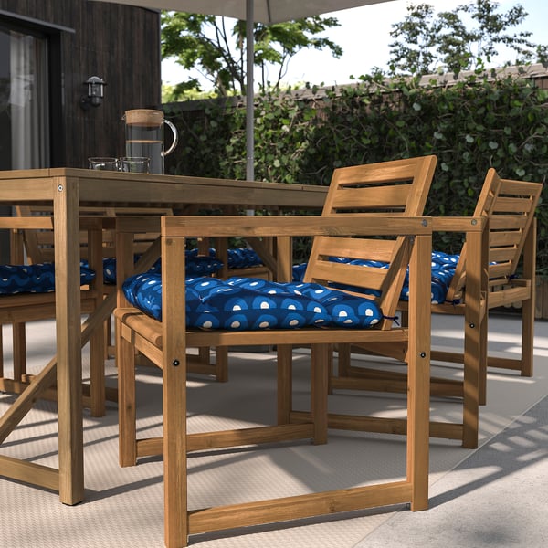 Terrassengarnitur mit rechteckigem Tisch, 4 Holzstühlen, blauen Kissen, Terrassengrün.